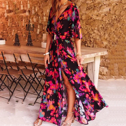 Frau in langem, buntem Blumenkleid vor rustikalem Holztisch und Steinwand.