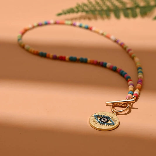 Bunte Perlenkette mit goldfarbenem Anhänger, Auge-Motiv, modisches Schmuckstück, Damenaccessoire.