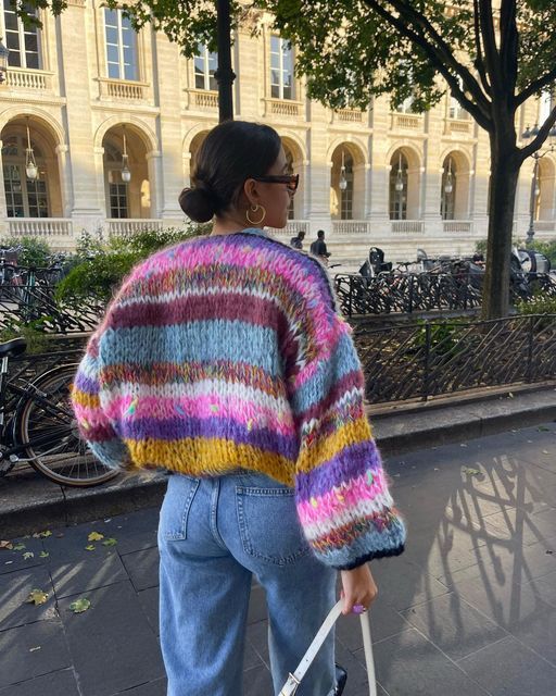 Frau in bunter Strickjacke und Jeans spaziert in der Stadt, Herbstmode, Streetstyle.