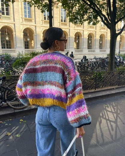 Frau in bunter Strickjacke und Jeans spaziert in städtischer Umgebung, Herbstmode, Streetstyle.