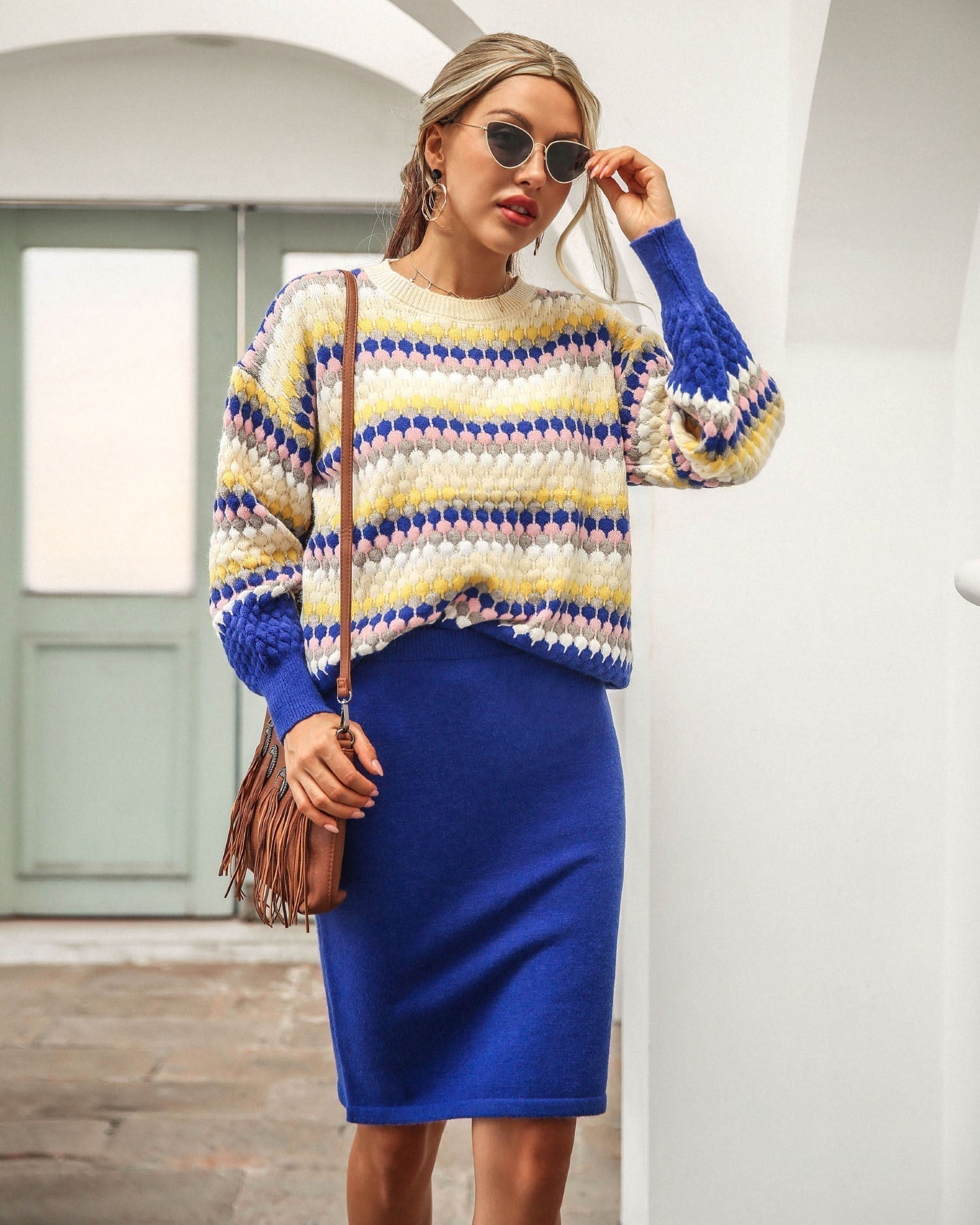 Frau in blauem Strickrock und gestreiftem Pullover, Sonnenbrille, braune Umhängetasche.