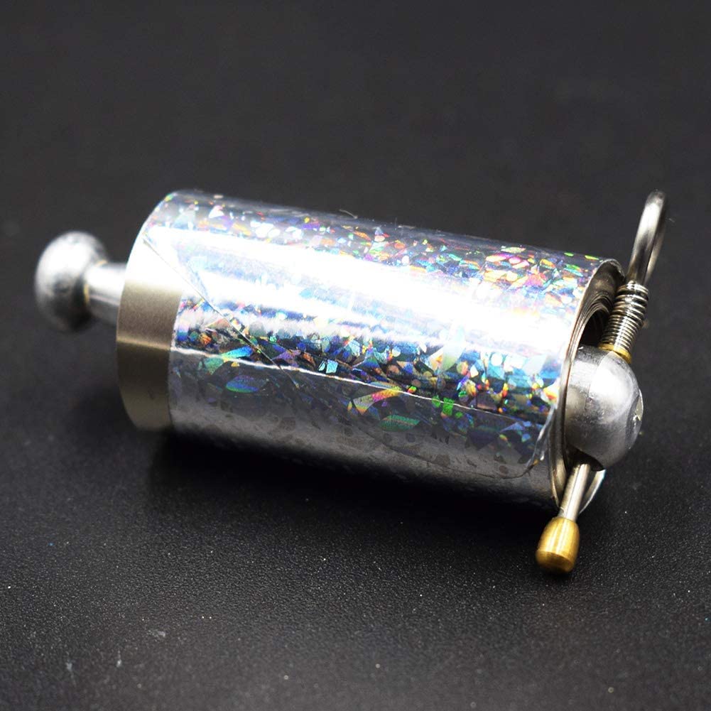 Nahaufnahme der aufgerollten Stabrolle mit holografisch schimmernder Folie, Metallknauf, Feder, Ring und goldenem Stift auf 5