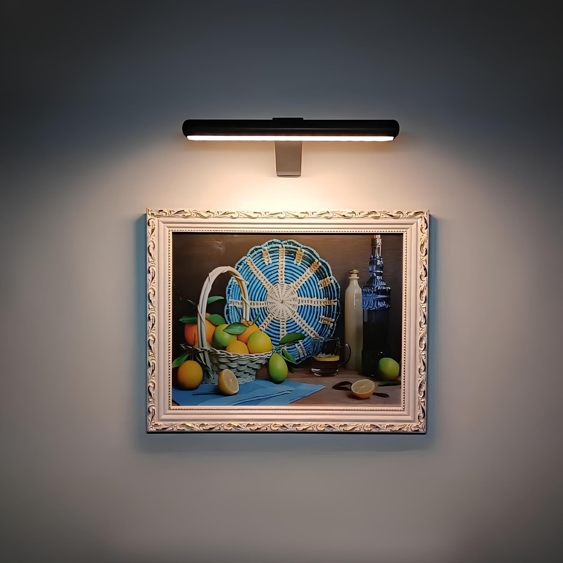Gemälde mit Obstkorb, Zitronen, Flasche und blauem Fächer, beleuchtet, im dekorativen Rahmen.