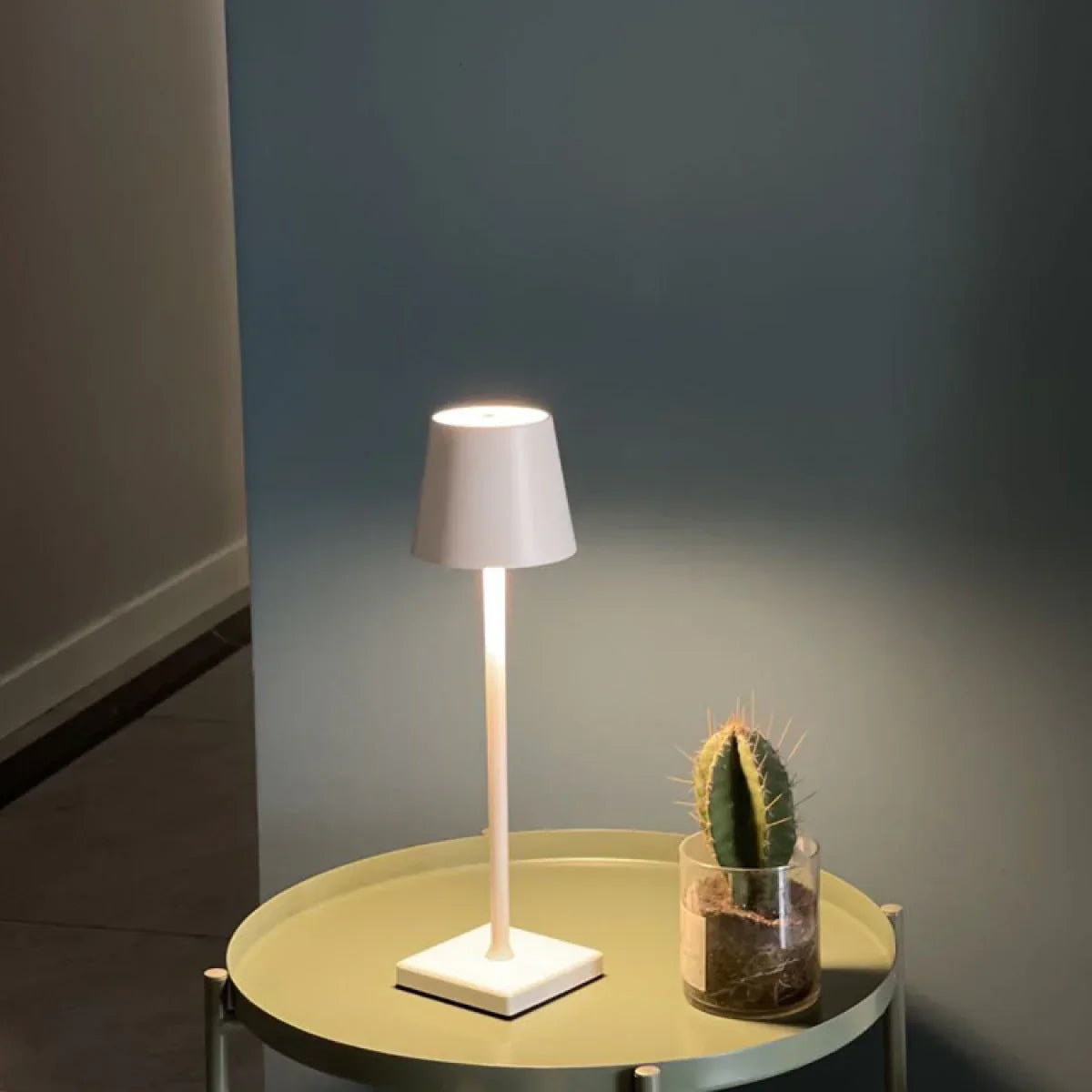 Weiße Tischlampe auf rundem Tisch neben kleinem Kaktus, modernes Design, Innenbeleuchtung.
