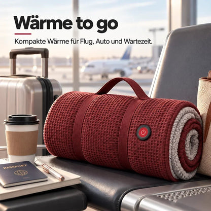 Aufgerollte rote Heizdecke mit Griff liegt am Flughafen auf einem Sitz, daneben Reisepass, Kaffeebecher und Koffer 12
