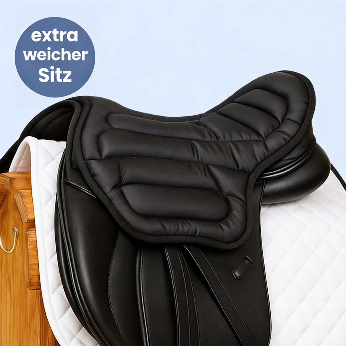 Schwarzes, gepolstertes Sitzkissen liegt auf einem schwarzen Dressursattel mit weißer Schabracke vor hellblauem Hintergrund 1