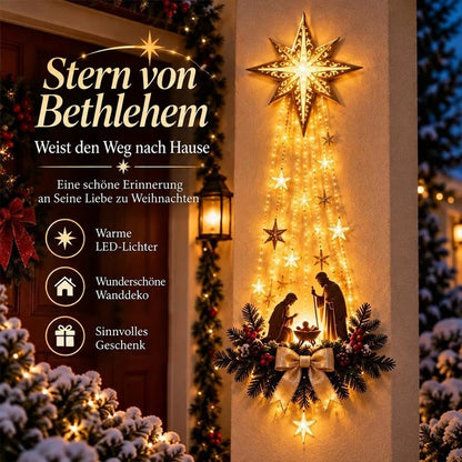 Leuchtender Stern mit herabhängenden Lichterketten und Krippenszene an einer Hauswand neben der Tür bei Schnee 1