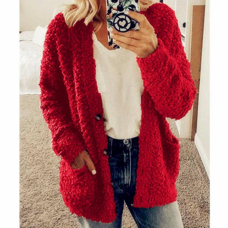 Frau in rotem Strickcardigan, weißem T-Shirt und Jeans, hält Smartphone, modische Herbstkleidung.