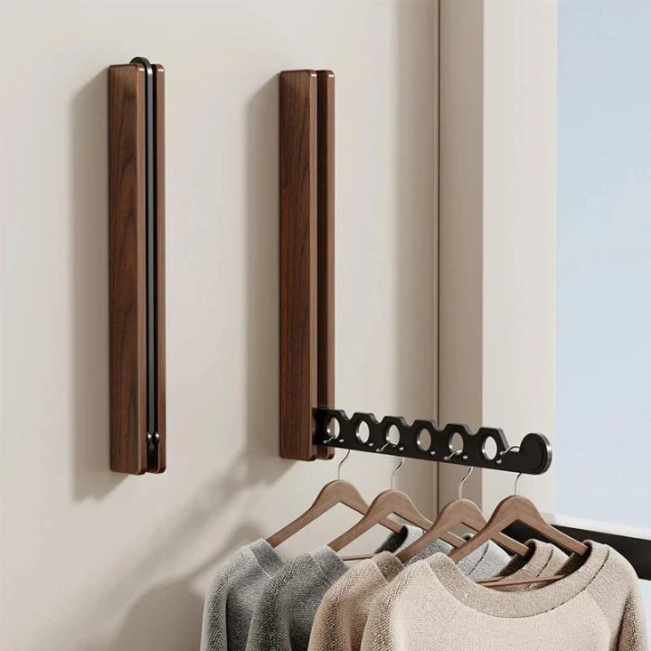 Zwei dunkle Holzhalter an der Wand, einer eingeklappt, einer ausgeklappt mit schwarzem Arm und vier Pullovern auf Holzbügeln. 7