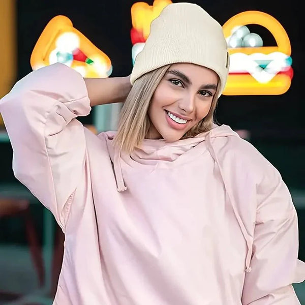 Lächelnde Frau trägt eine cremefarbene Beanie zu einem rosa Kapuzenpullover vor leuchtenden Neonmotiven 2