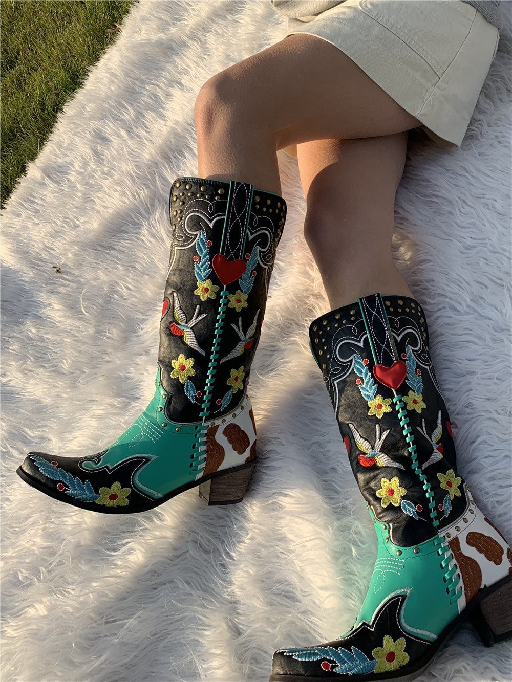 Farbige Cowboy-Stiefel mit Blumenmuster auf weißem Teppich, Damenmode, Westernstil.