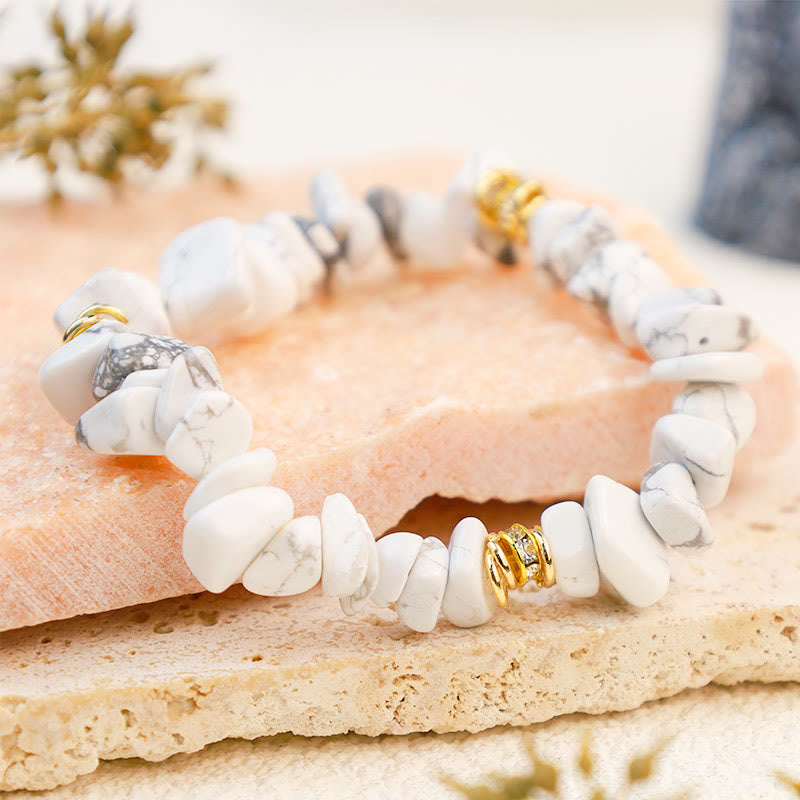 Armband aus weißen Howlith-Steinen mit goldenen Akzenten auf beigem Hintergrund.