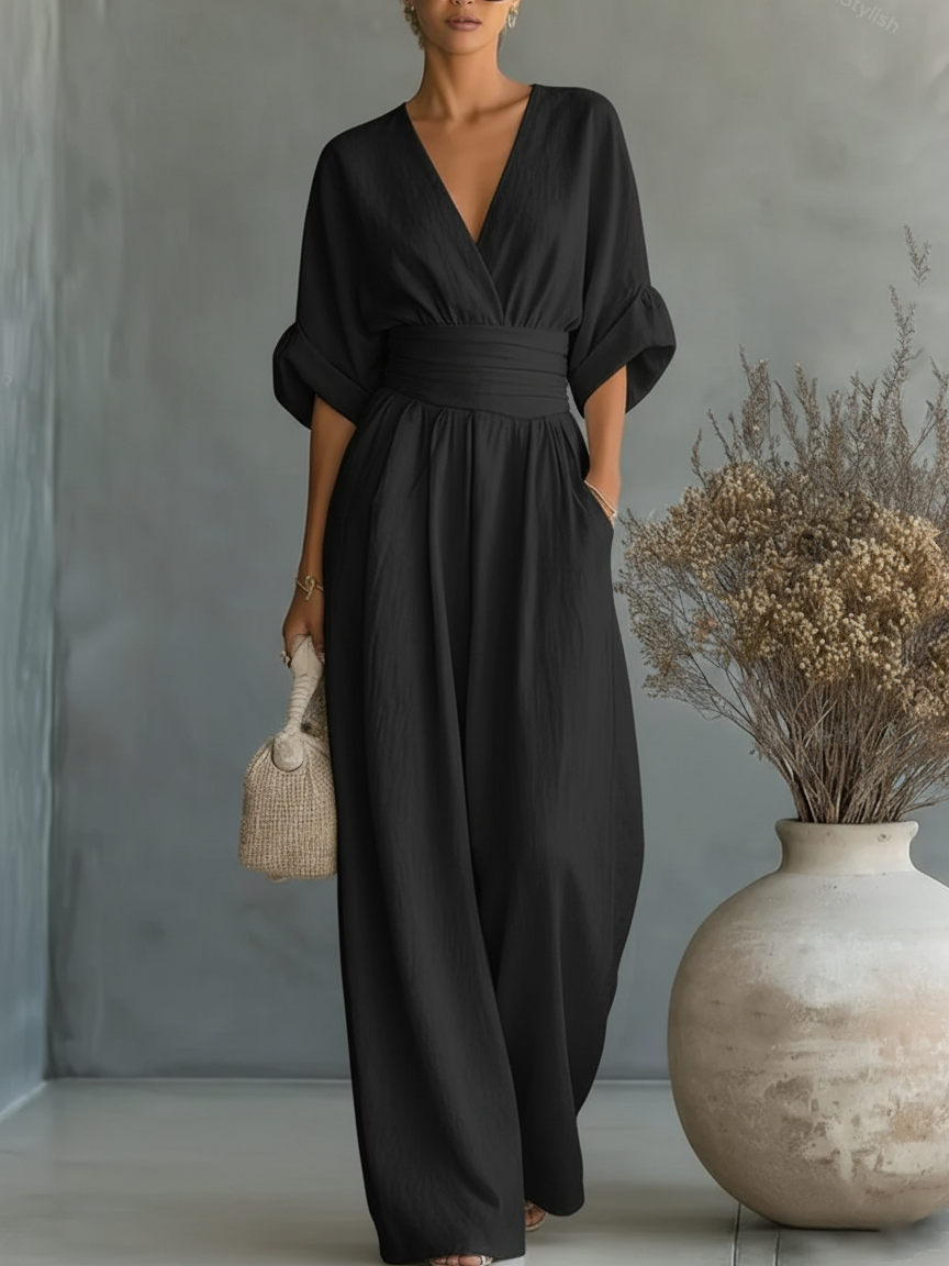 Model trägt den Jumpsuit in Schwarz, die Hand in der Seitentasche, daneben eine große Vase mit Trockenblumen 4
