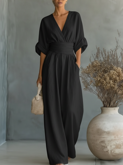 Model trägt den Jumpsuit in Schwarz, die Hand in der Seitentasche, daneben eine große Vase mit Trockenblumen 4