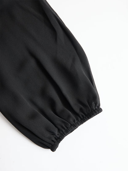 Nahaufnahme des schwarzen, durchscheinenden Puffärmels mit elastischem Bündchen, flach auf weißem Hintergrund ausgelegt. 4