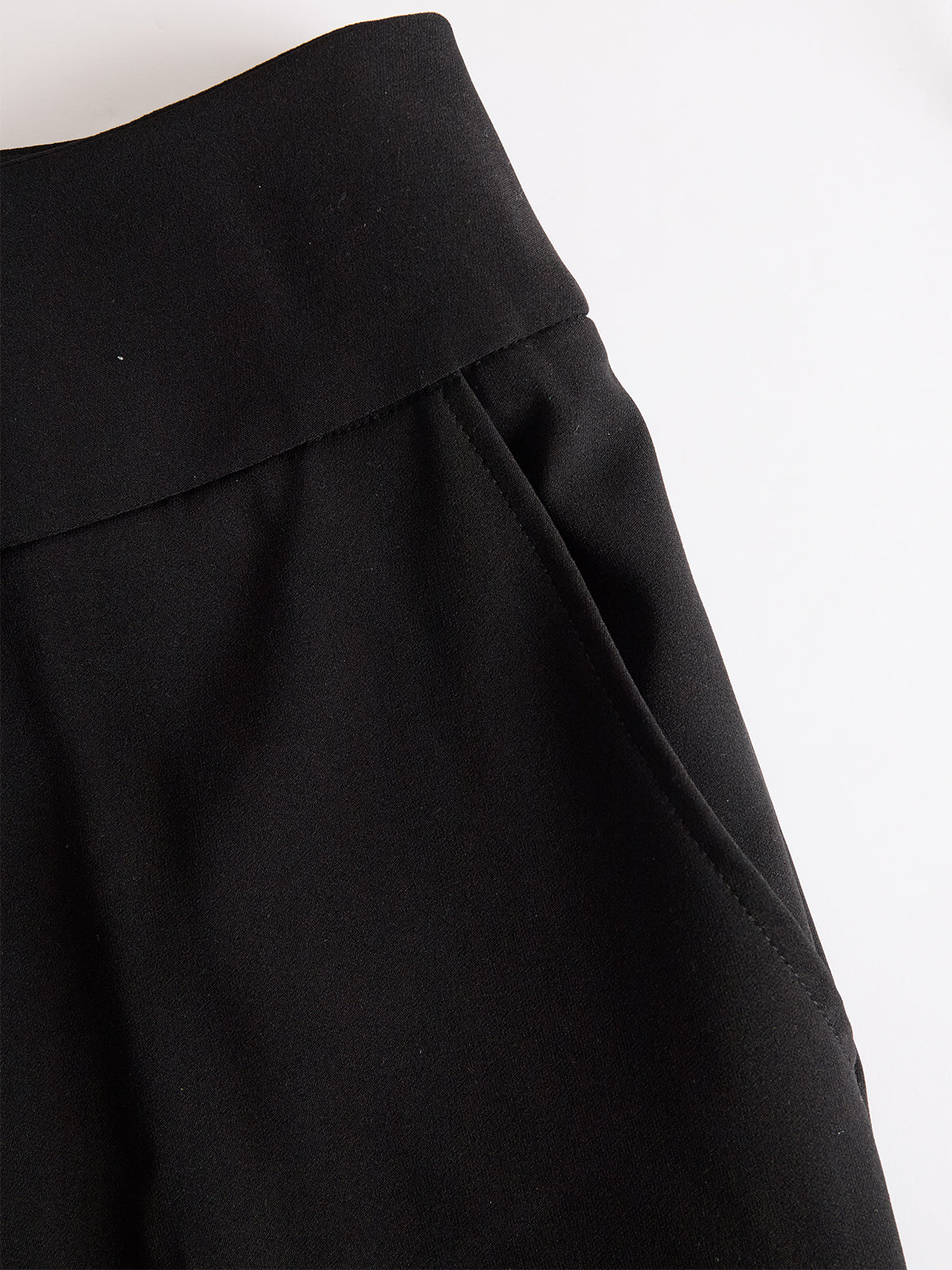 Detailaufnahme der schwarzen Hose mit breitem Bund und eingearbeiteter Seitentasche, flach auf hellem Hintergrund. 5