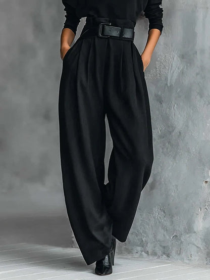 Detailansicht der schwarzen Hose mit weitem Bein, Bundfalten und breitem Gürtel, Hände in den Seitentaschen 4
