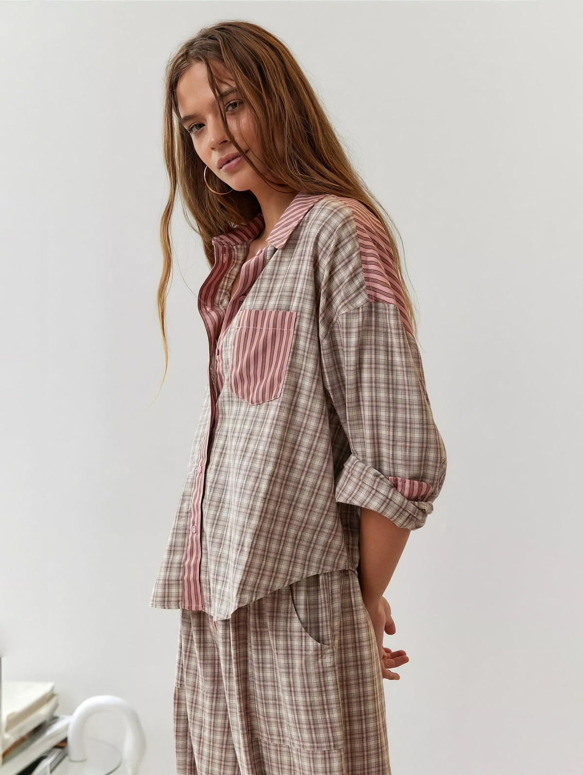 Model im rosa-beige karierten Pyjama-Set mit rosa gestreiftem Kragen und aufgesetzter Brusttasche, seitlich gedreht, die Arme hinter dem Rücken. 2
