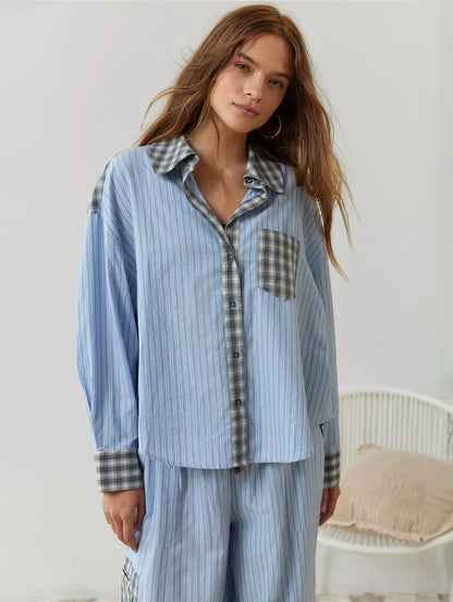Frontansicht des blau gestreiften Pyjama-Hemds mit grau karierten Manschetten, Kragen und Brusttasche, geschlossen getragen, daneben ein Korbstuhl. 5
