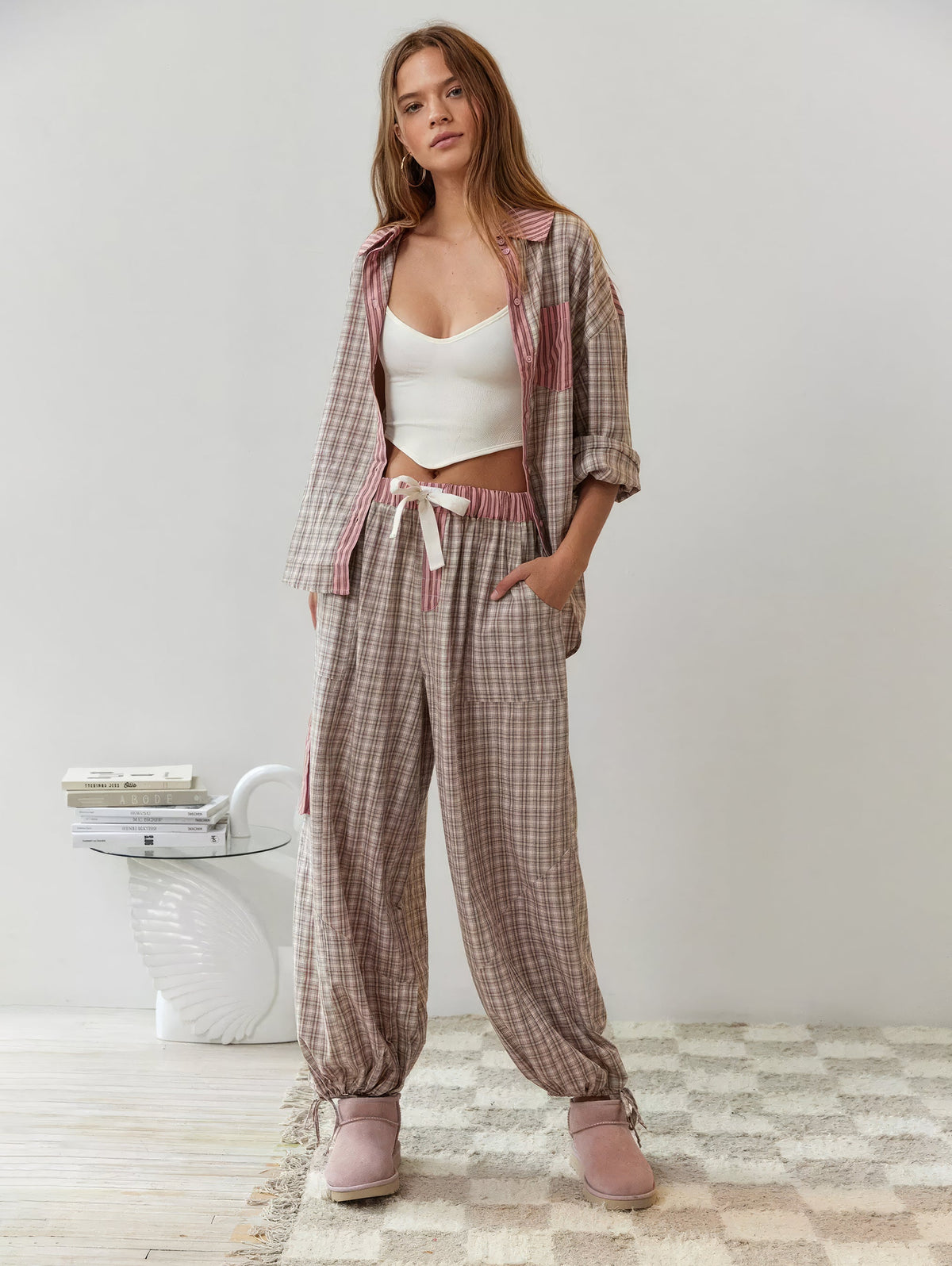 Ganzkörperbild im rosa-beige karierten Pyjama-Set: offenes Hemd über weißem Top, weite Hose mit Kordelzug und Bündchen an den Knöcheln. 6