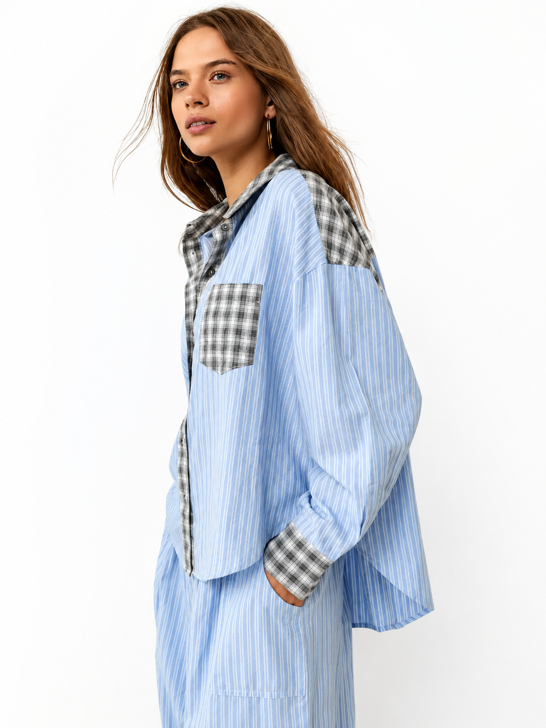 Seitenansicht des blau gestreiften Pyjama-Hemds mit grau-weiß kariertem Kragen, Brusttasche und Manschetten, getragen von einem Model, Hand in der Hosentasche. 1