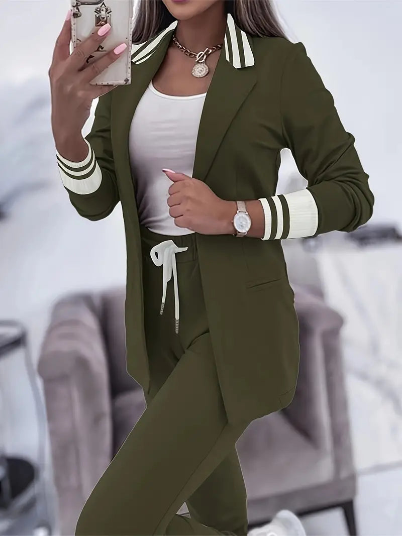Frau in olivgrünem Jogginganzug mit Blazer, weißem Top, Smartphone und Uhr im Wohnzimmer.