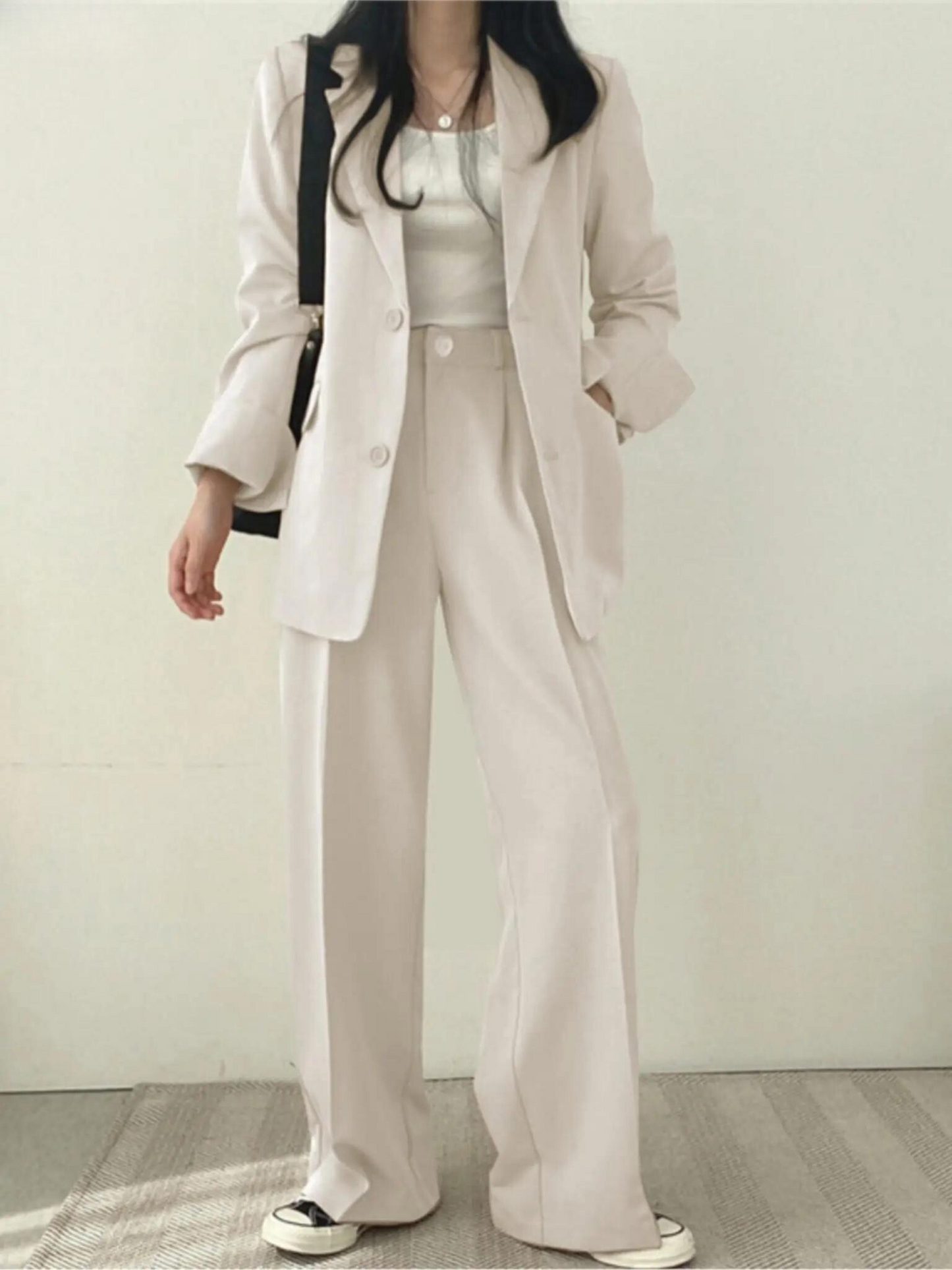 Frau in cremefarbenem Anzug mit weißem Top und Sneakers, modisch, elegant, Büro-Outfit.