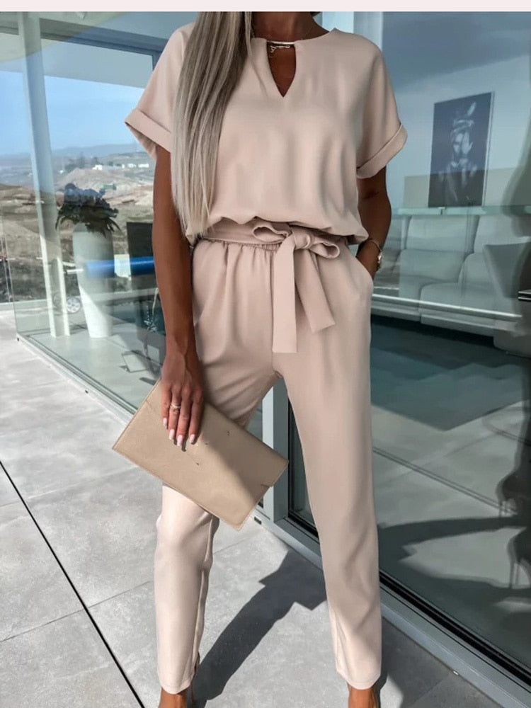 Frau in beigem Jumpsuit mit Gürtel, hält beigen Clutch, moderne Mode, eleganter Look.