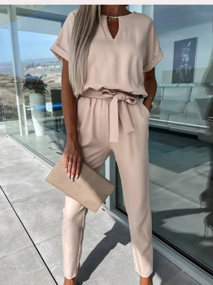 Frau in beigem Jumpsuit mit Gürtel, hält beigen Clutch, moderne Mode, eleganter Look.