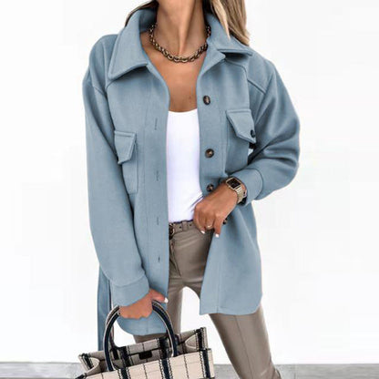 Frau in blauer Jacke, weißem Top, beigen Hosen, hält karierte Handtasche, modisch, elegant.