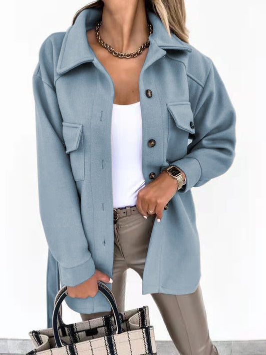 Frau in hellblauer Wolljacke, weiße Bluse, beige Hose, kariertes Handtasche, modisch elegant.