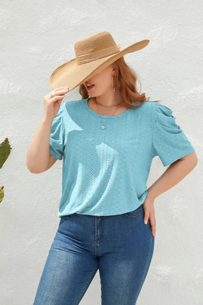 Frau mit Strohhut, blauer Spitzenbluse und Jeans vor weißer Wand.
