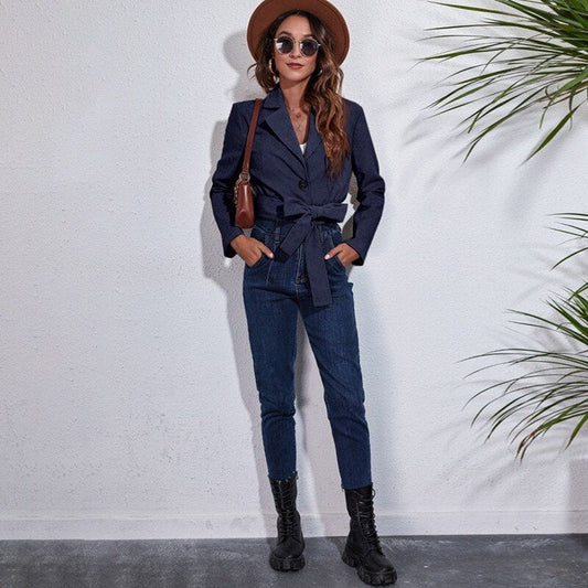 Frau in dunkelblauem Blazer und Jeans, brauner Hut, Sonnenbrille, schwarze Stiefel, modisch.