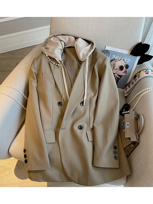 Beiger Blazer mit Kapuze, Doppelreiher, Damenmode, eleganter Stil, auf Sessel drapiert.