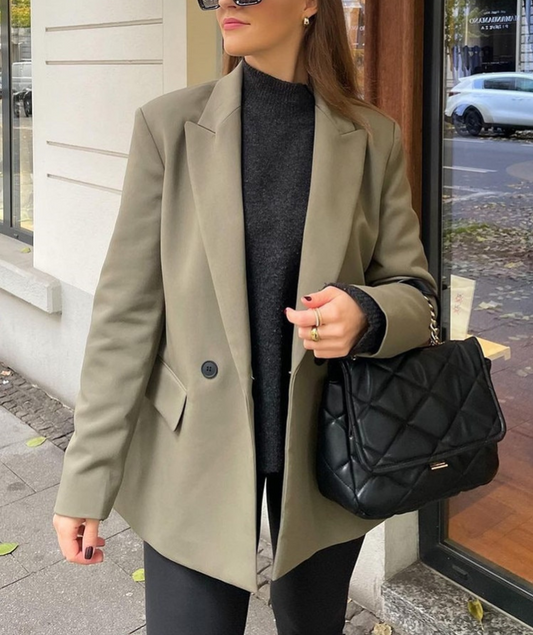 Frau in beigem Blazer mit schwarzer Stepphandtasche auf Straße.