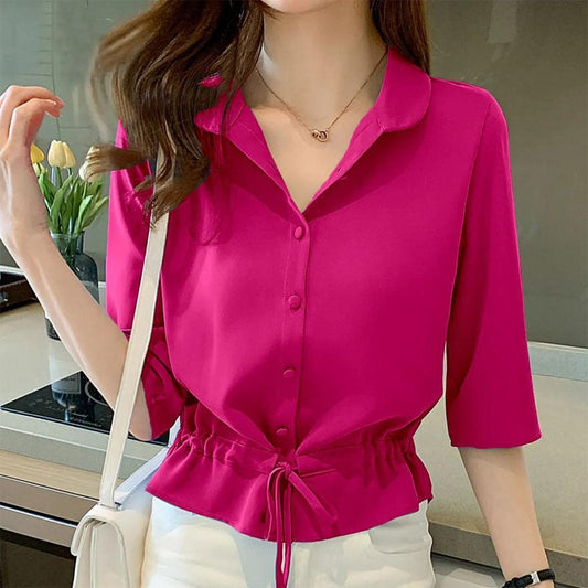 Frau in pinker Bluse mit Kordelzug, weiße Hose, Tulpen im Hintergrund, modisch, elegant.