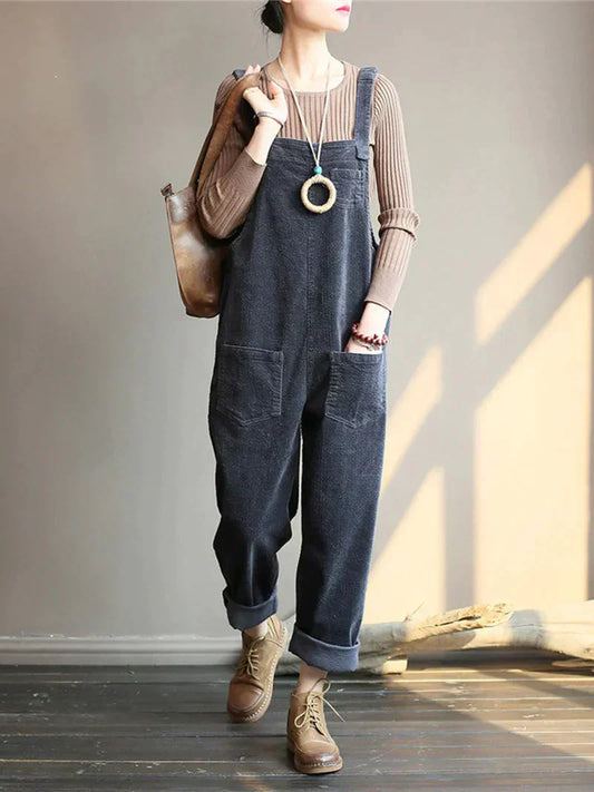 Frau in grauem Cord-Overall, braunem Pullover, Lederstiefeln und Tasche, modisch, lässig.