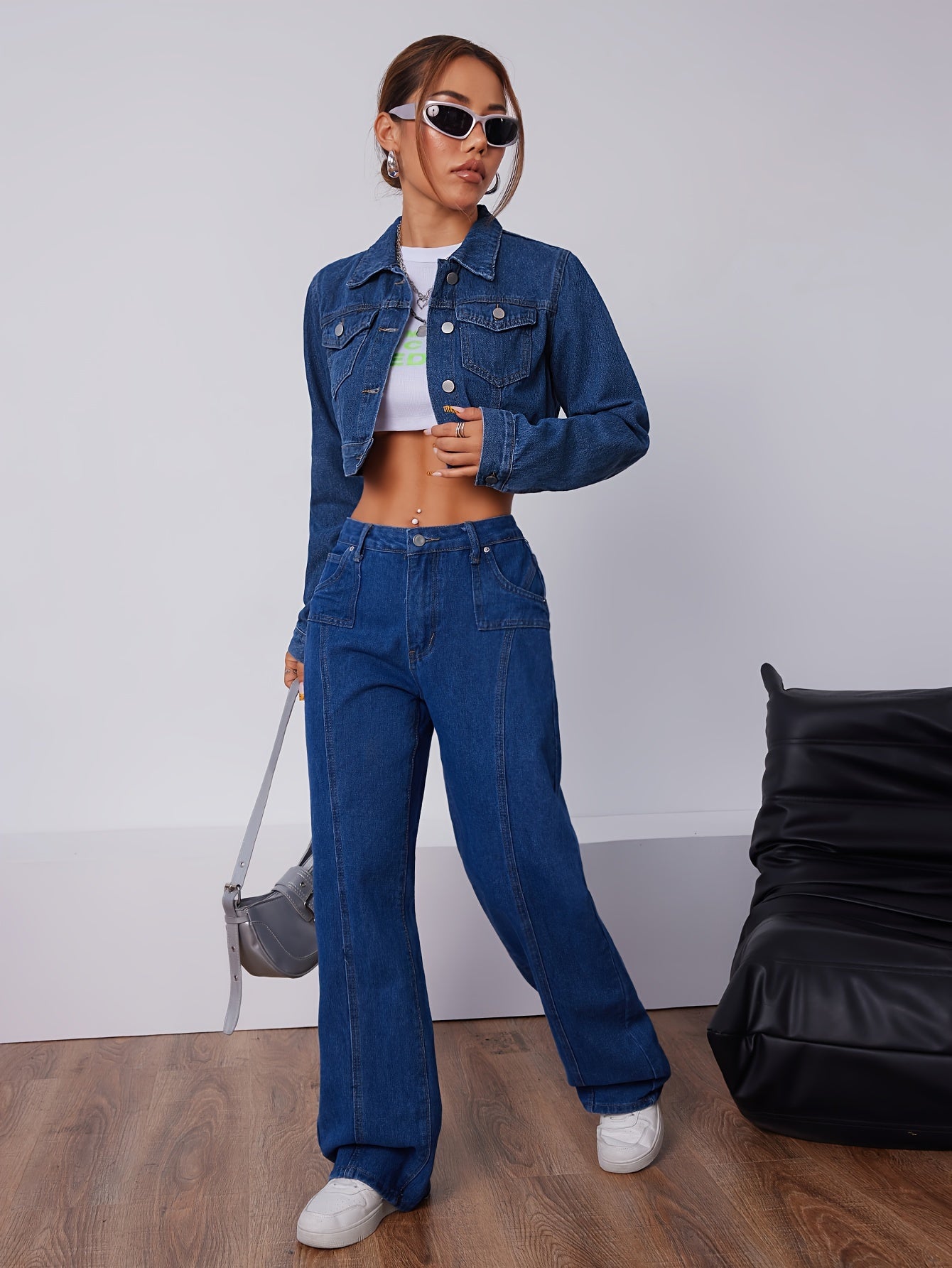 Frau in blauer Jeansjacke und Jeanshose, weißes Crop-Top, Sonnenbrille, modisch, lässig.