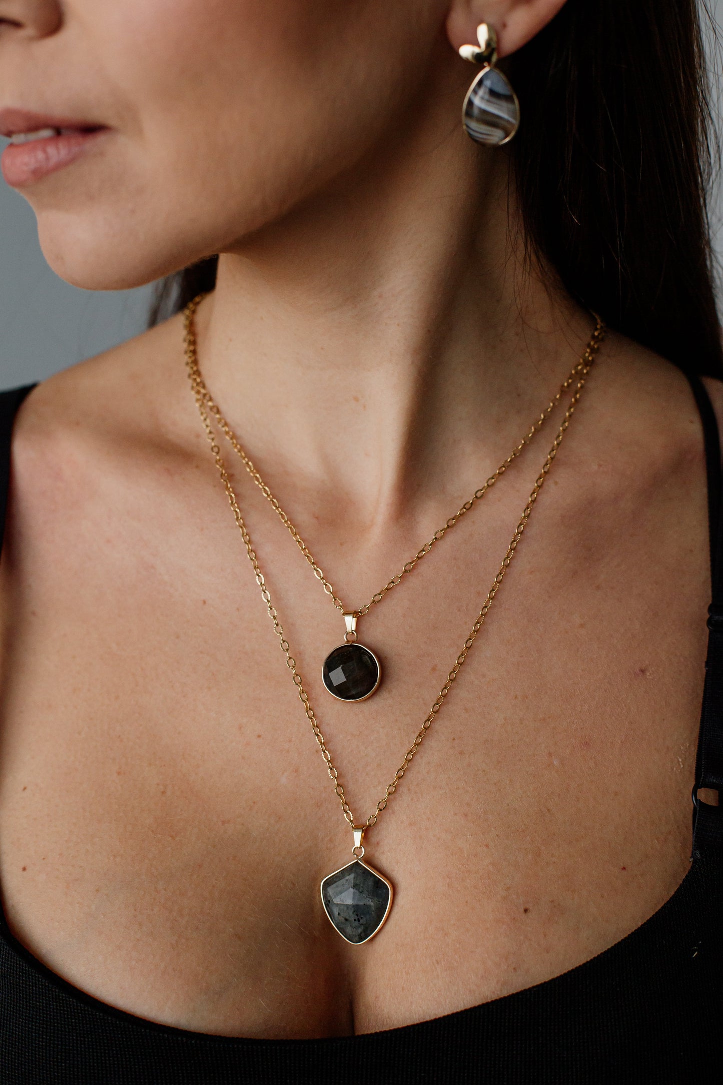 Frau mit goldener Halskette und Ohrringen, schwarzer Anhänger, eleganter Schmuck, Nahaufnahme.