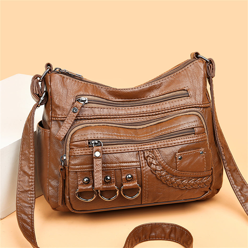 Braune Lederhandtasche mit Reißverschlusstaschen und dekorativen Ringen, Damenmode Accessoire.