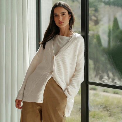 Frau trägt weißen Strick-Cardigan, lässig, elegant, vor Fenster stehend, Herbstmode.