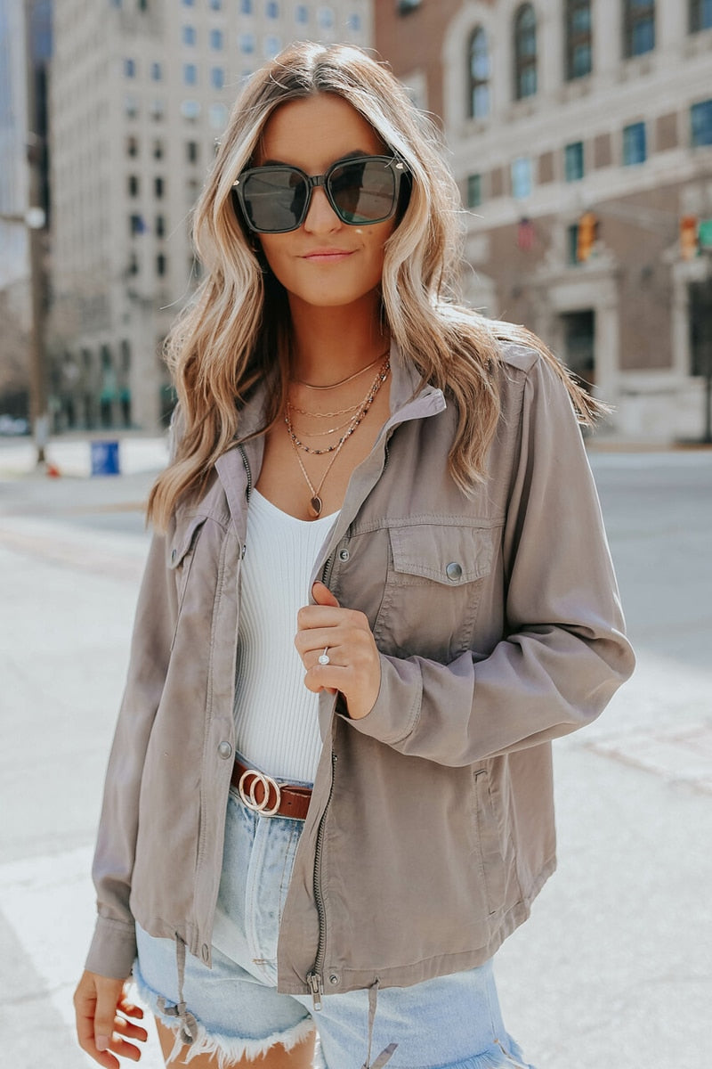 Frau in grauer Jacke und Sonnenbrille, lässiger Streetstyle, modische Damenbekleidung.