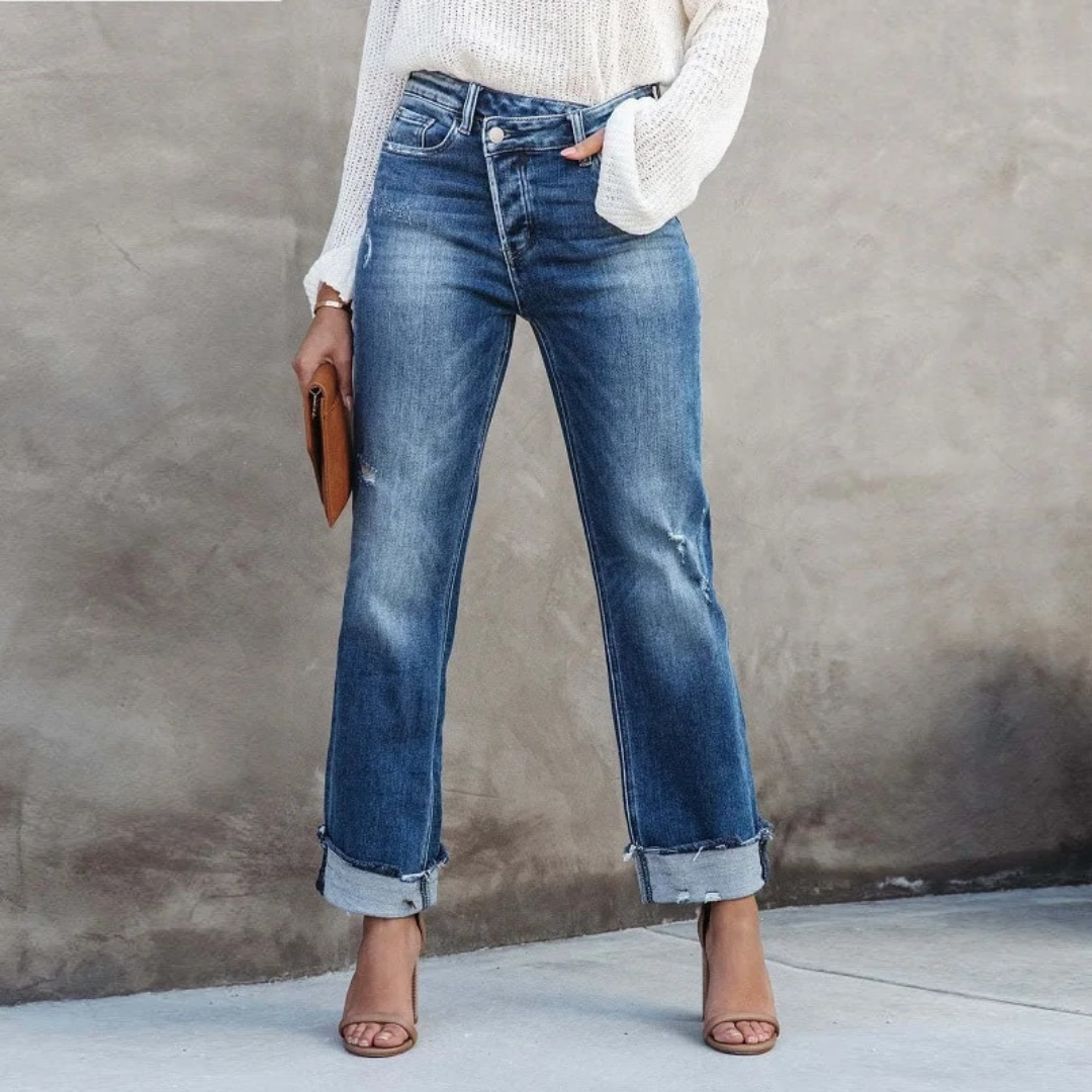 Frau in blauer Jeans und weißem Pullover, hält braune Clutch, trägt Sandalen.