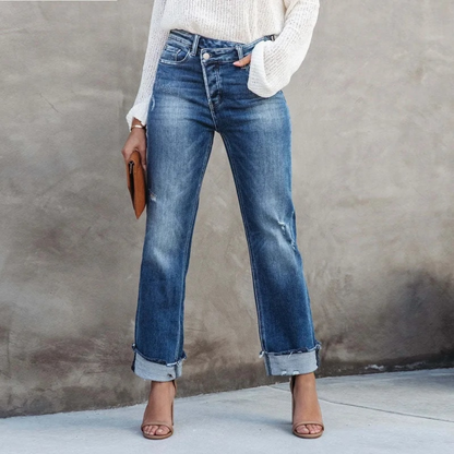 Frau in blauer Jeans und weißem Pullover, hält braune Clutch, trägt Sandalen.