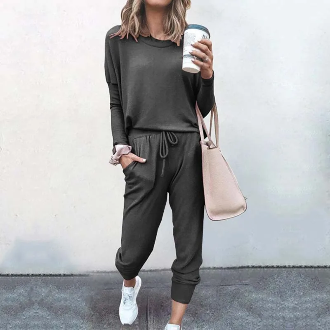 Frau in grauem Jogginganzug mit Kaffeebecher und rosa Tasche, lässige Damenmode.