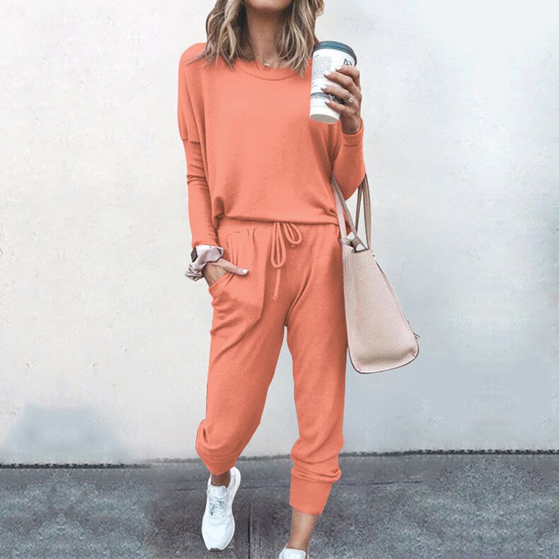 Frau in orangefarbenem Jogginganzug mit Kaffeebecher und Handtasche, lässige Mode.