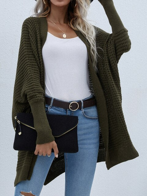 Frau in olivgrünem Strickcardigan, weißem Top, Jeans, mit schwarzer Clutch.