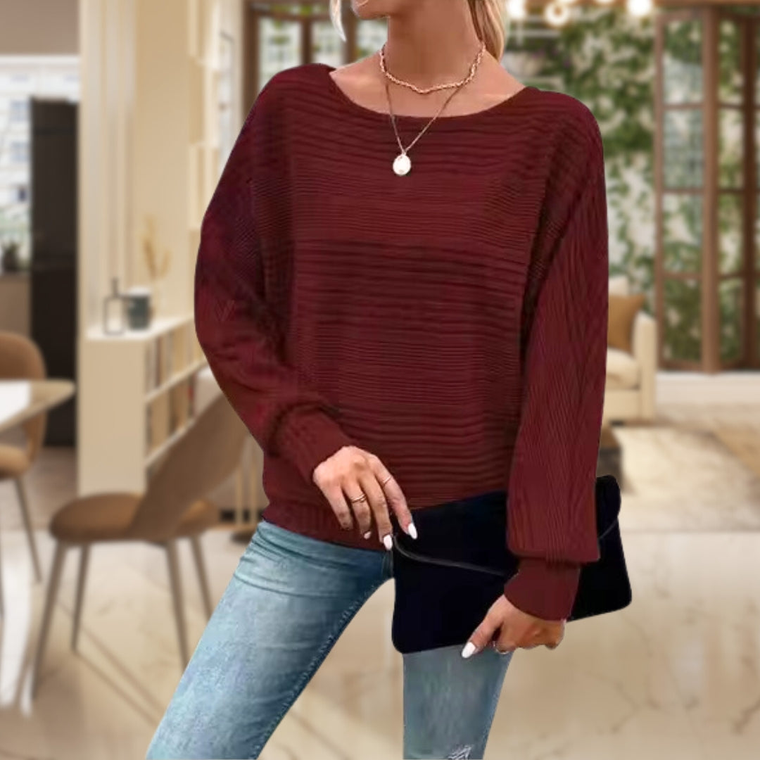 Frau in rotem Strickpullover, blaue Jeans, schwarze Clutch, modernes Wohnzimmer.