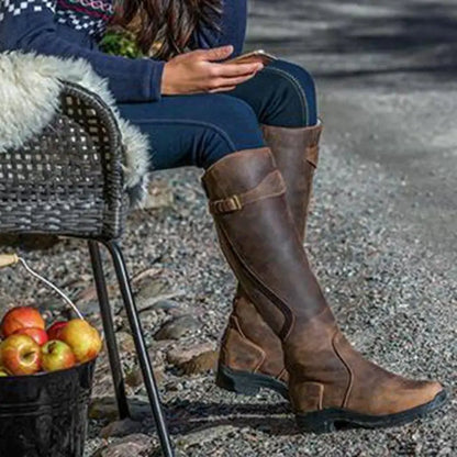 Frau mit braunen Lederreitstiefeln, sitzt auf Stuhl, Herbst, Äpfel im Eimer, Outdoor-Szene.