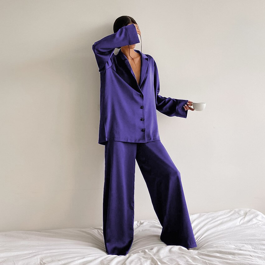 Frau in lila Satin-Pyjama-Anzug mit Kaffeetasse, moderne Nachtwäsche, Schlafzimmer.